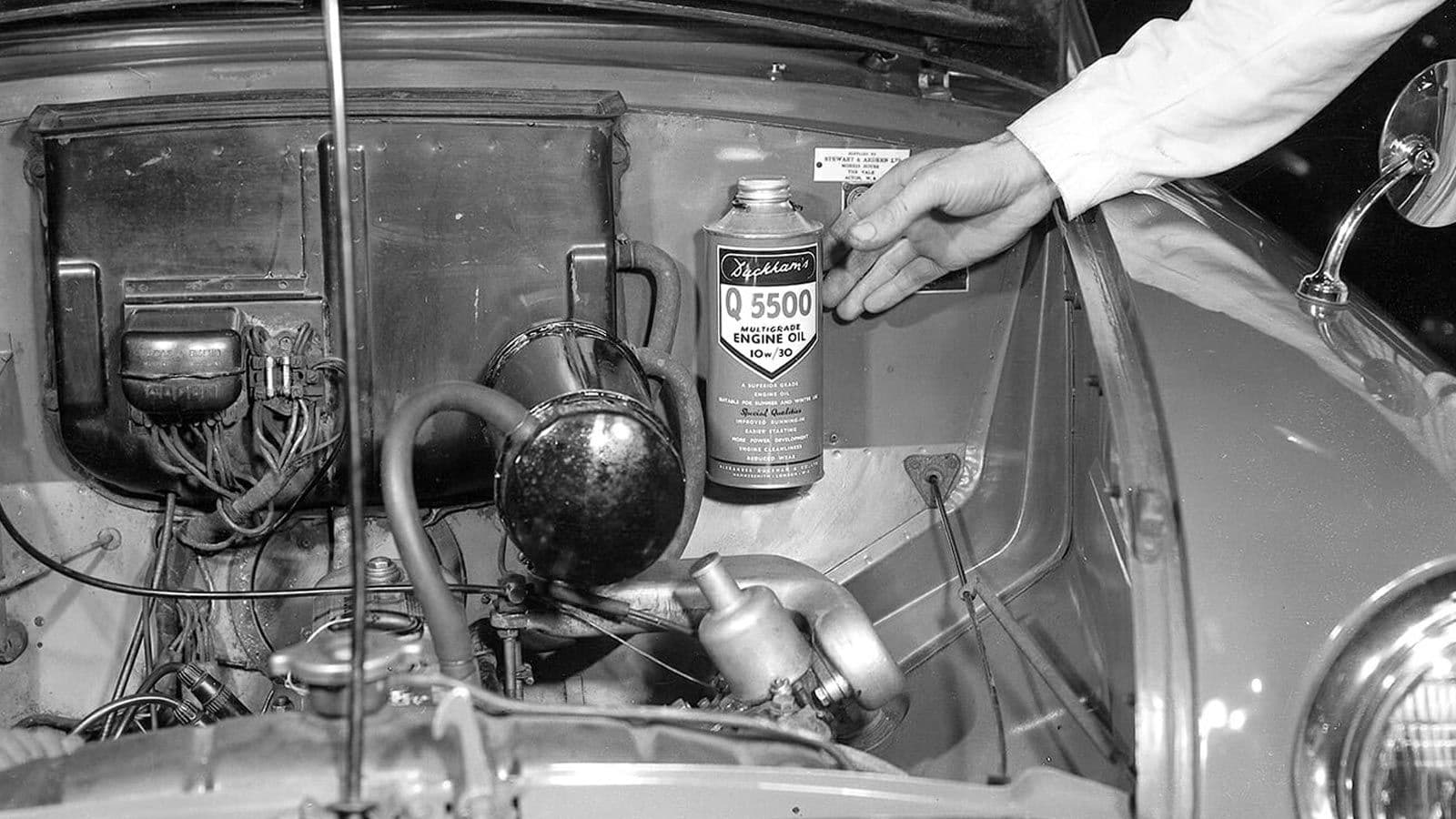 A hand setting a can of Duckhams Q 5500 multigrade engine oil onto the engine of a car, photographed in 1951