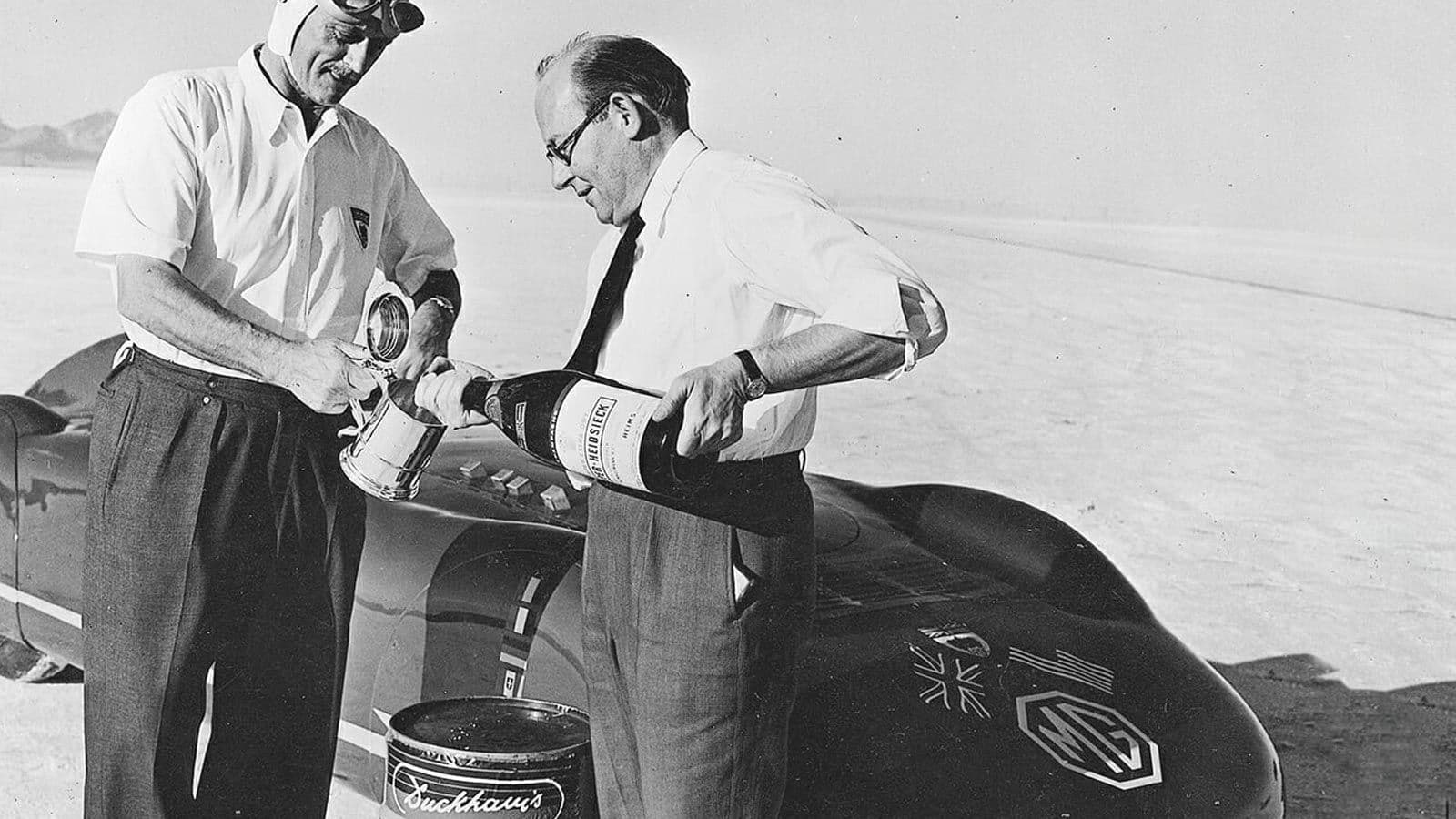 Two men in shirtsleeves pouring oil into a record car on the Utah salt flats.